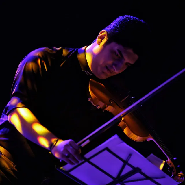 Kasra Kaveh playing violin under stage lighting.